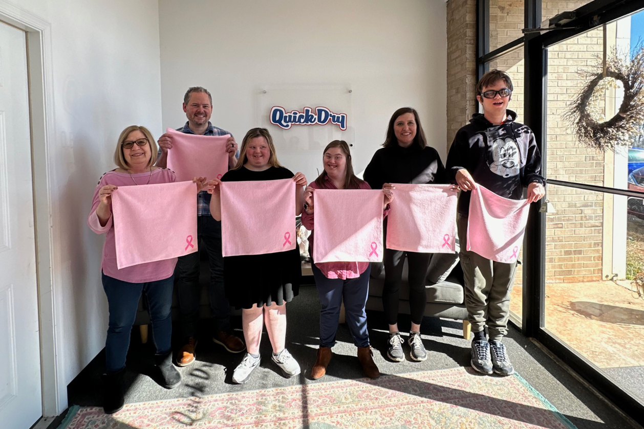 A group of people holding up pink Quick Dry towels
